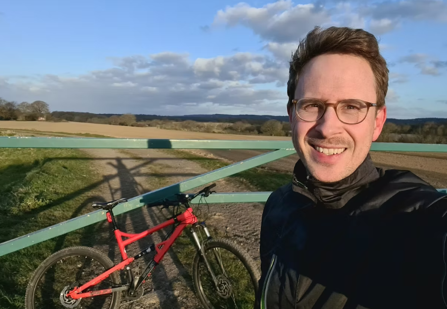 Ben James profile selfie next to red bicycle and green gate